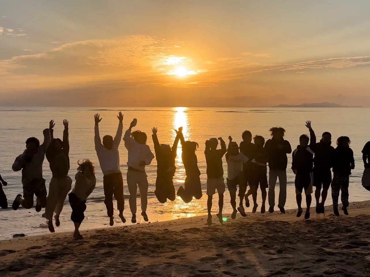 夕日のビーチでジャンプするスタッフたち